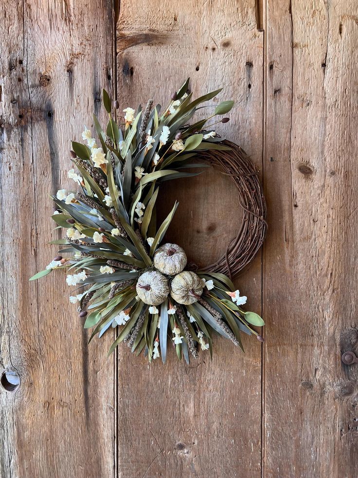 a wreath hanging on the side of a wooden door with white flowers and greenery