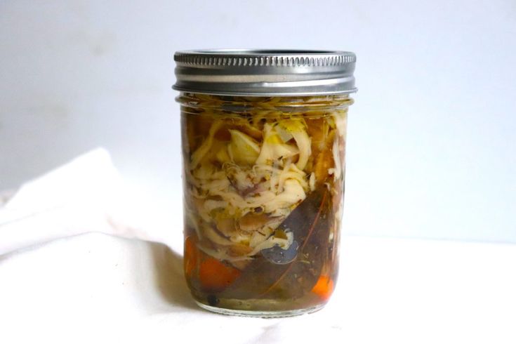 a glass jar filled with pickled vegetables on top of a white cloth covered table