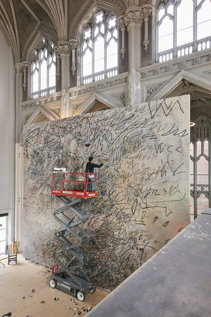 a man on a scaffolding machine in front of a large painting