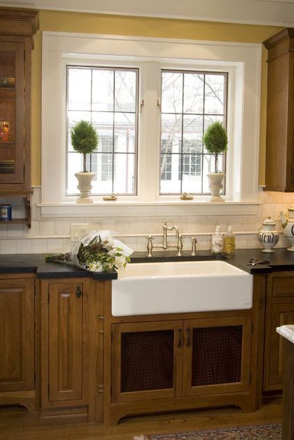 a kitchen with wooden cabinets and black counter tops, two large windows above the sink