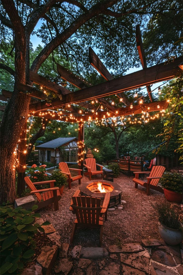 an outdoor fire pit surrounded by wooden chairs and trees with lights strung over it's sides