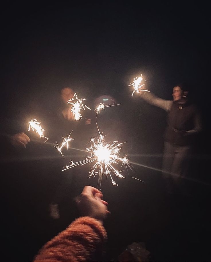 people holding sparklers in the dark with one person pointing at them and another person looking up