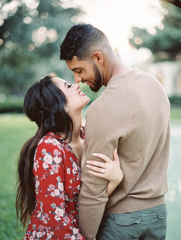 a man and woman standing next to each other in front of a tree with the sun shining down on them