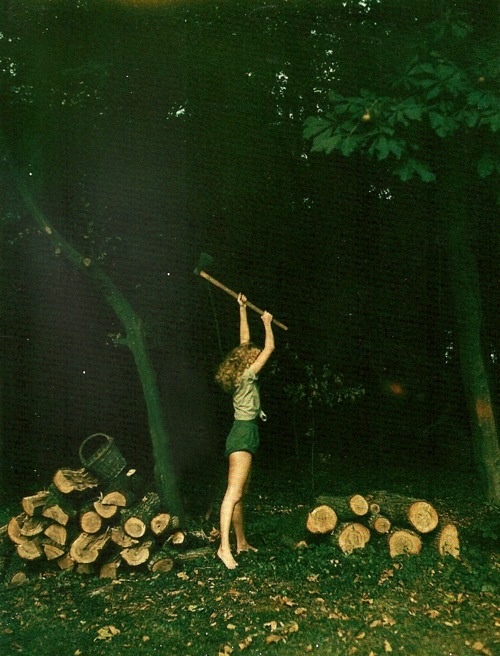 a woman holding a stick above her head while standing in front of a pile of logs