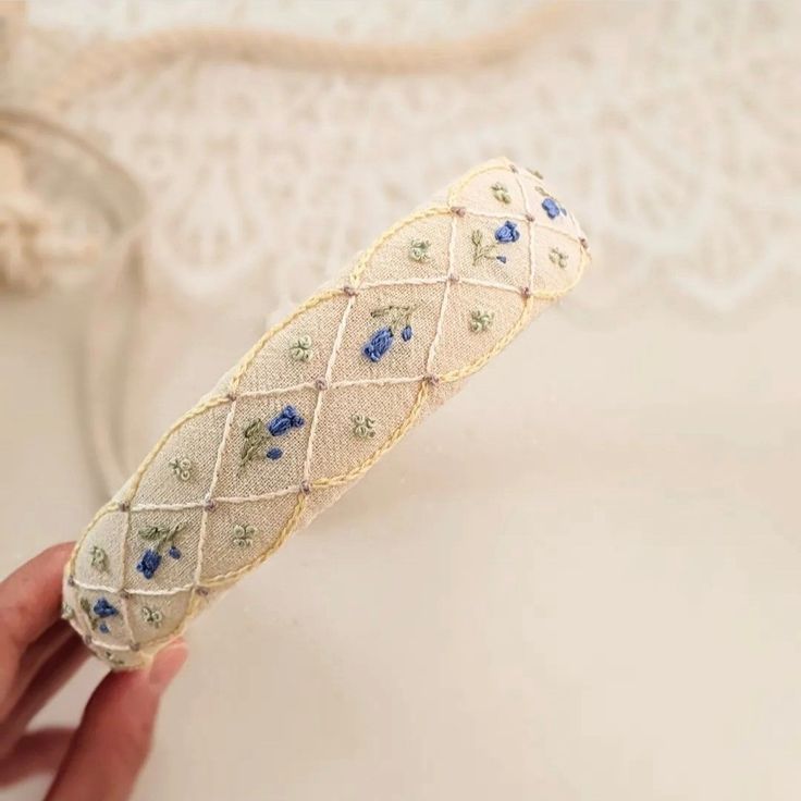 a hand holding a piece of cloth with blue flowers on it and lace around the edge