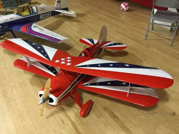 a red, white and blue model airplane on a wooden floor with other toy planes in the background