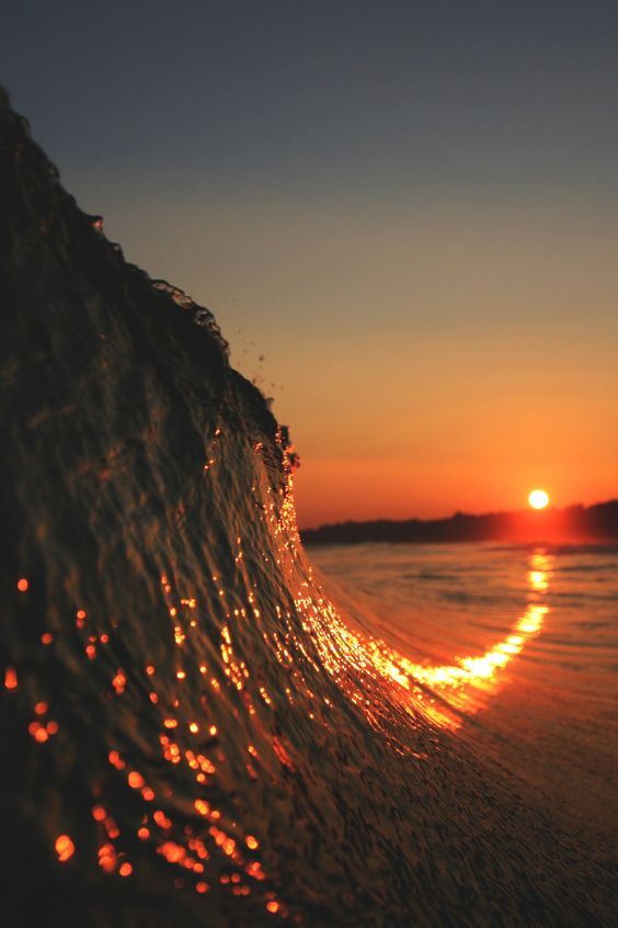 the sun is setting behind a wave in the ocean