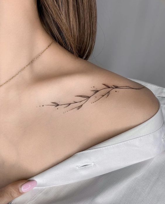 the back of a woman's shoulder with a small branch tattoo on her left shoulder