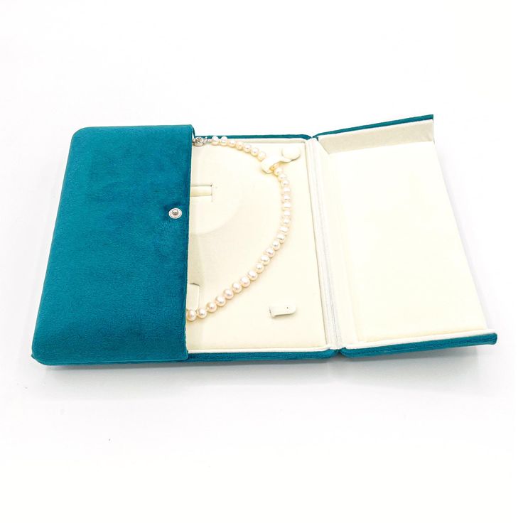 an open blue book with a pearl necklace on the front and inside it, sitting on a white surface