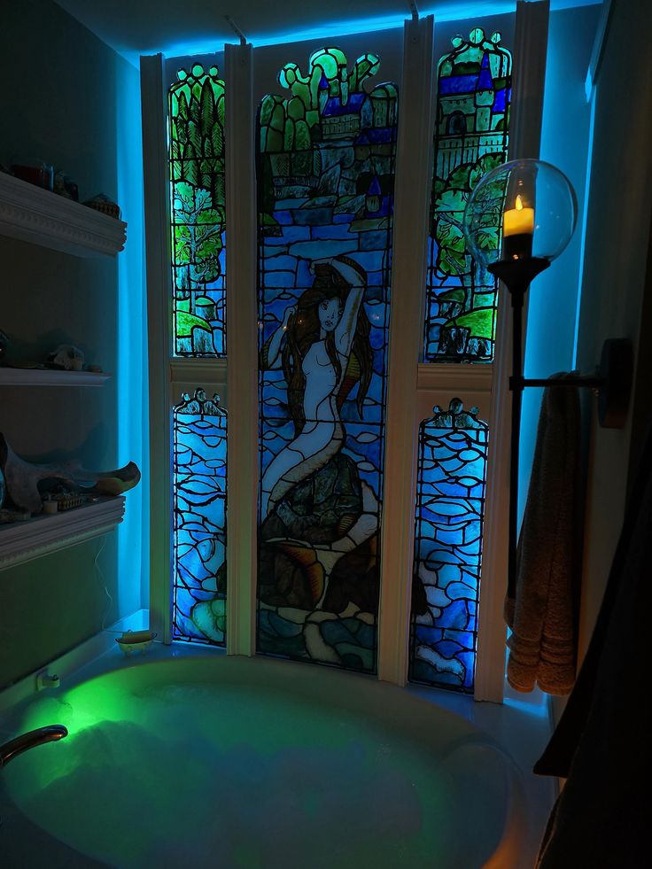 a bath tub sitting under a stained glass window next to a candle and book shelf