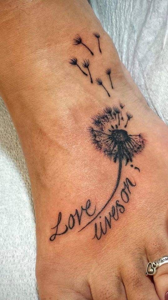 a foot with a dandelion tattoo on it that says love is in the air