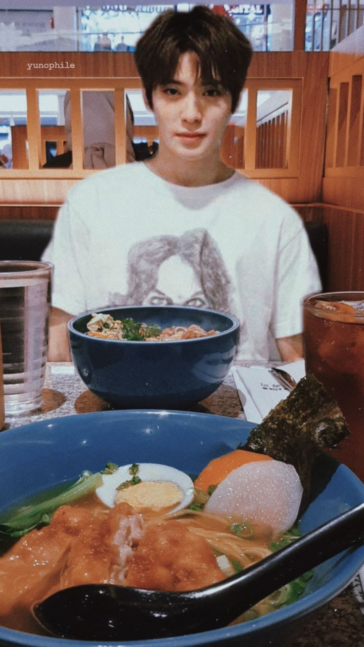 a young man sitting at a table with food in front of him and a bowl of soup to the side