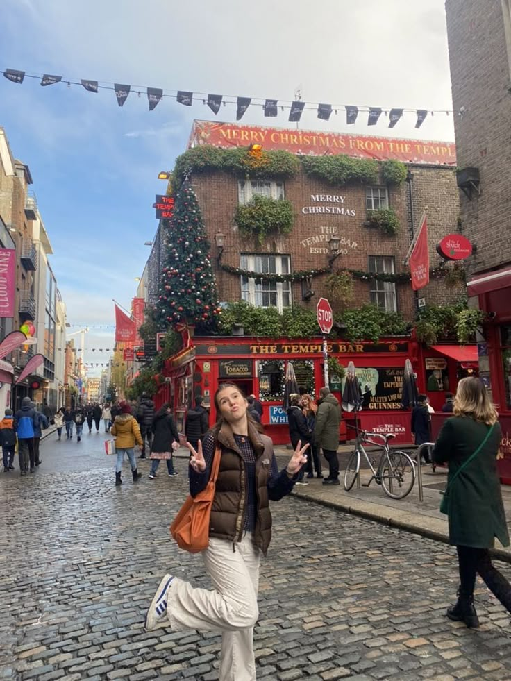 a woman standing in the middle of a cobblestone street with people walking around