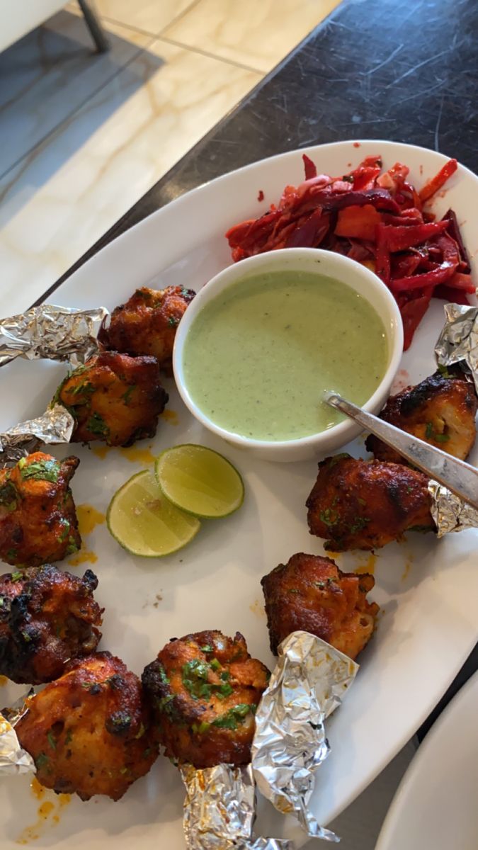 a white plate topped with meat and vegetables next to a bowl of dipping sauce on top of it