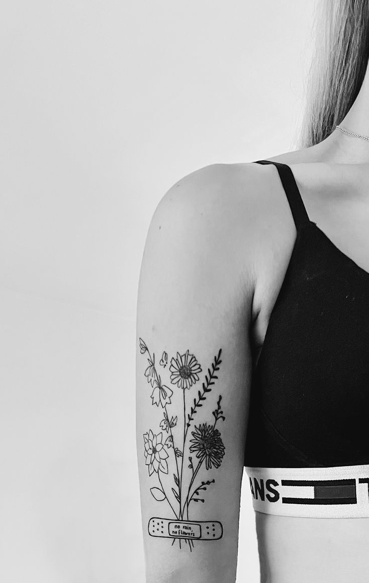 black and white photograph of woman with flower tattoo on her left arm, wearing sports bra