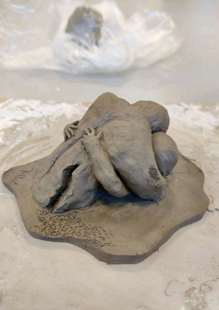 a clay sculpture of a person laying on top of a rock in the middle of sand