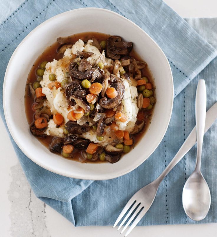 a white bowl filled with meat and veggies on top of a blue napkin