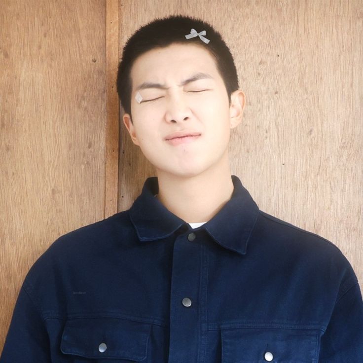 a man with his eyes closed standing in front of a wooden wall