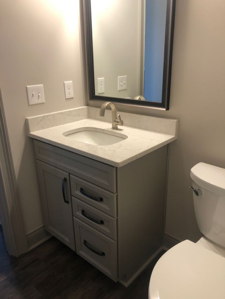 a white toilet sitting next to a sink in a bathroom under a large framed mirror