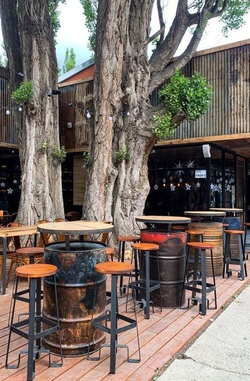 tables and stools are set up in front of the tree lined outdoor seating area