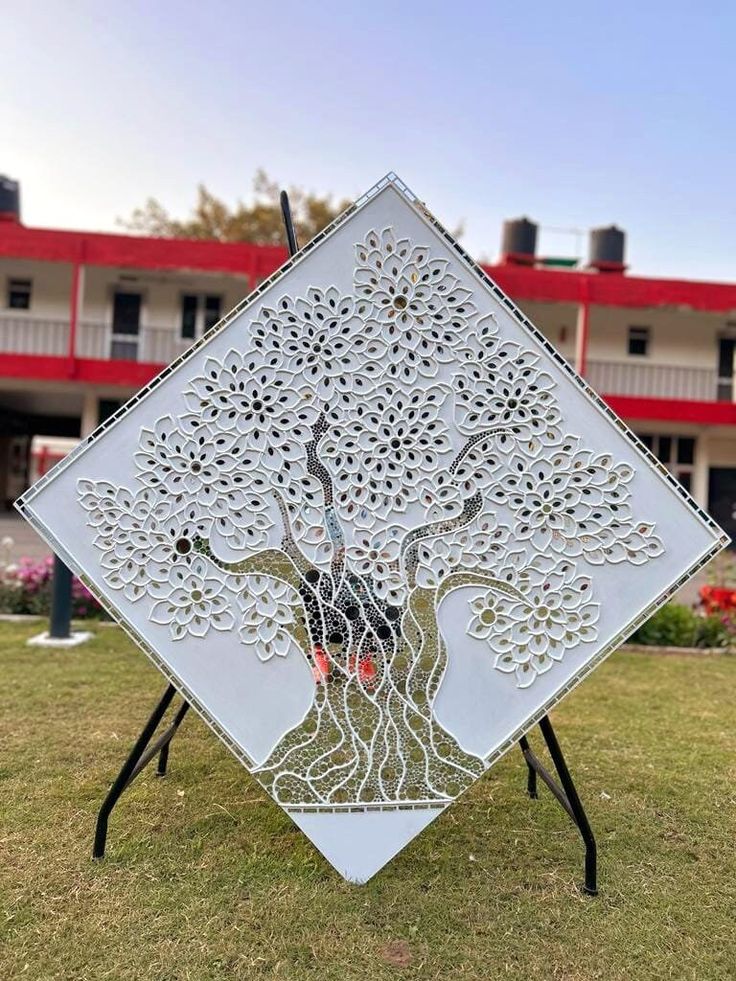 a metal sculpture with a tree on it in front of a red and white building