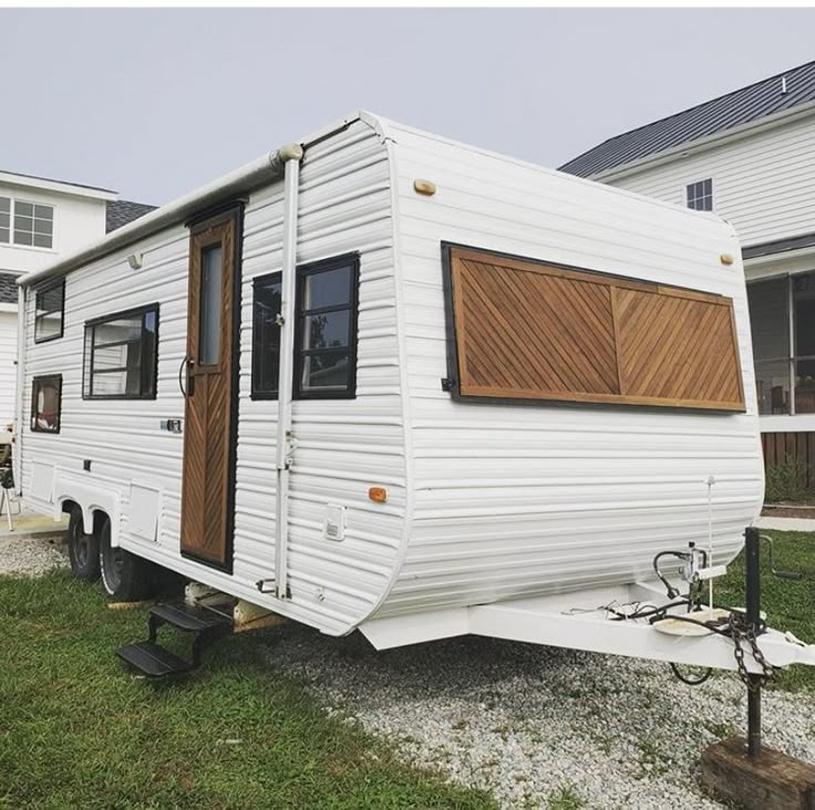 a white trailer parked on top of a green grass covered field next to a house