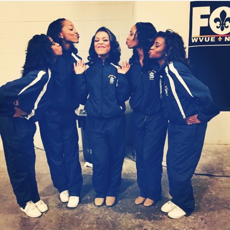 four women in black and white tracksuits are posing for a photo with their hands together