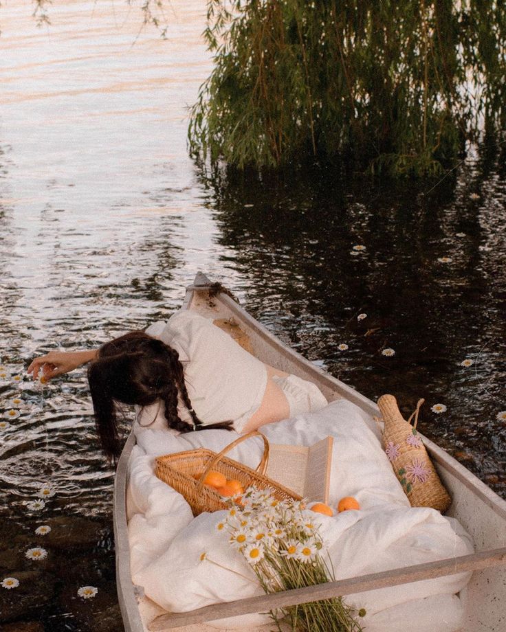 a woman laying in a boat on top of a lake next to a bunch of flowers