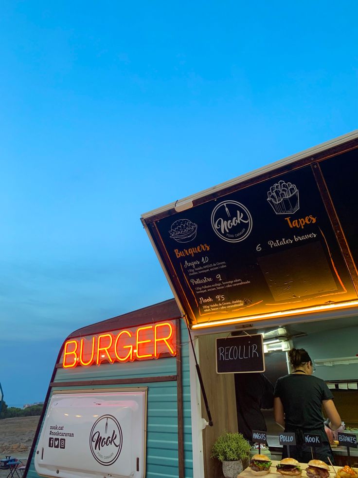 there is a man standing at the counter in front of a food truck that has burgers on it