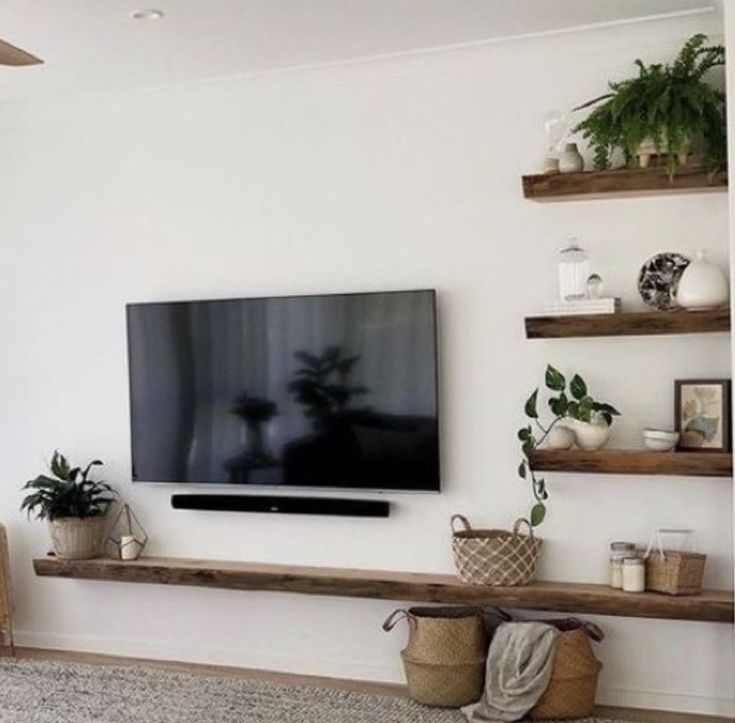 a flat screen tv sitting on top of a wooden shelf next to potted plants