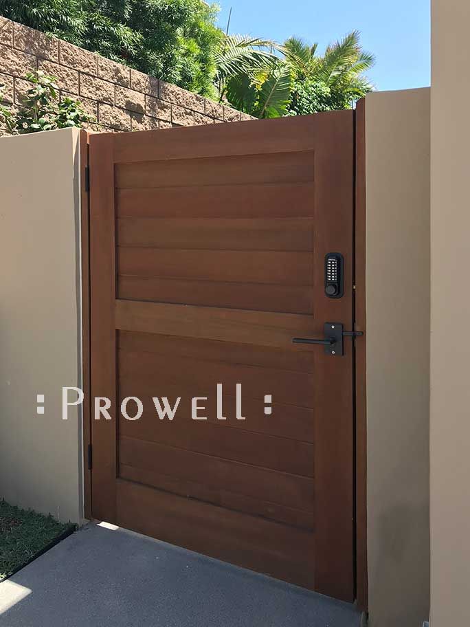 a brown wooden door in front of a white fence and brick wall with the words prowell written on it