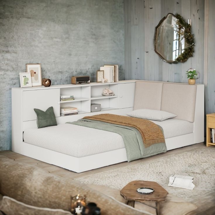 a white bed sitting next to a wooden table with a mirror on top of it