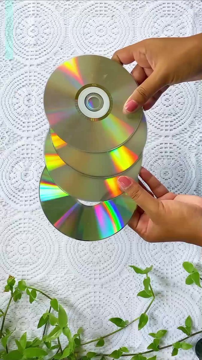 someone holding two cds in their hands on top of a white tablecloth with green leaves