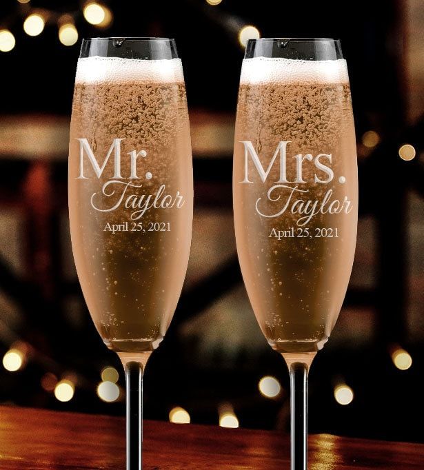 two champagne flutes sitting next to each other on top of a wooden table with lights in the background