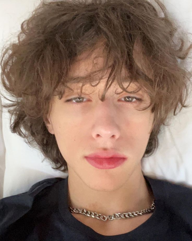 a close up of a person laying in a bed with a necklace on his neck