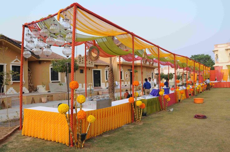 an outdoor event with tables covered in yellow and orange cloths, decorated with pom poms