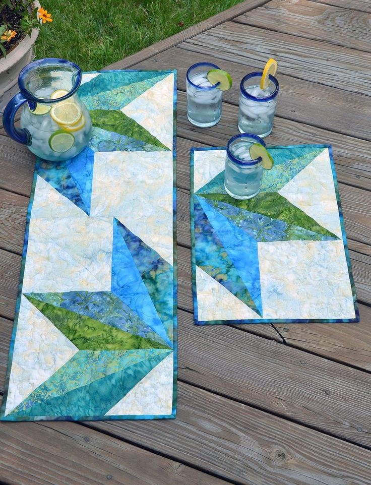 two quilted placemats sitting on top of a wooden table next to drinks