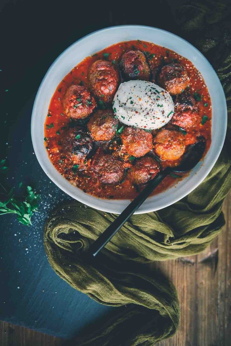 a white bowl filled with meatballs and sour cream on top of a wooden table