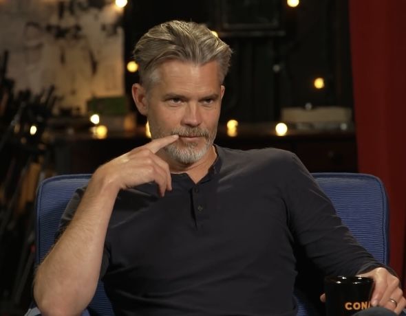 a man sitting in a blue chair holding a coffee cup and looking at the camera