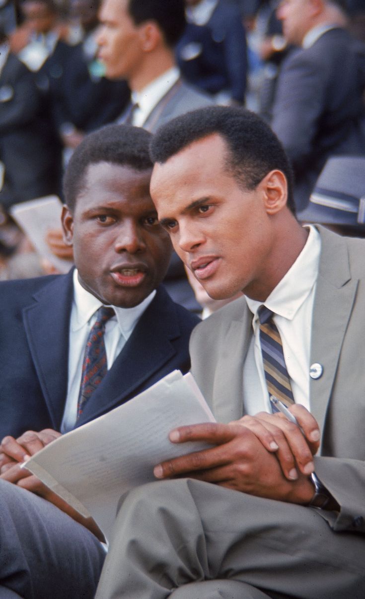 two men in suits sitting next to each other and looking at something on a clipboard