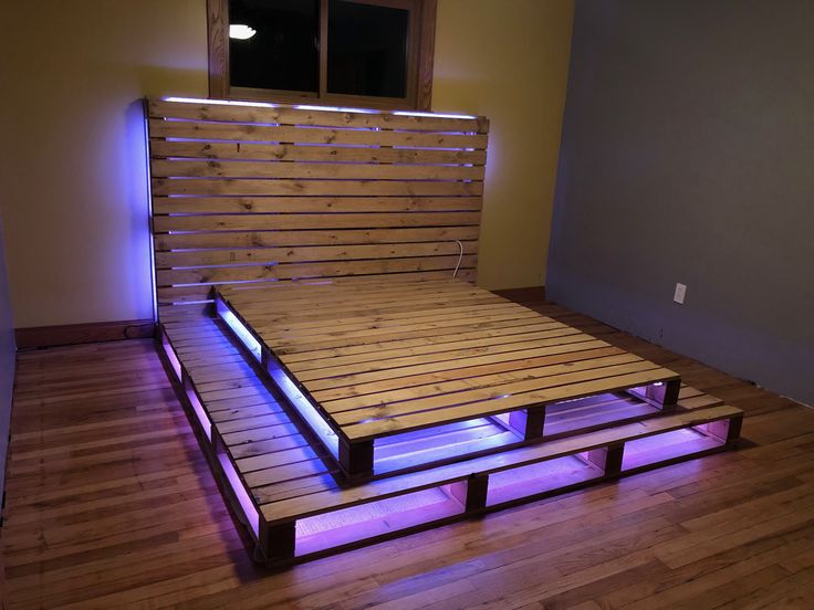 a bed made out of pallet wood with purple lights on the bottom and sides