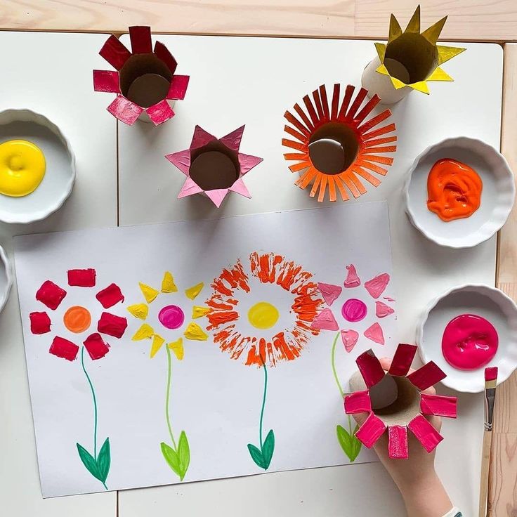 a child's hand is painting flowers on paper