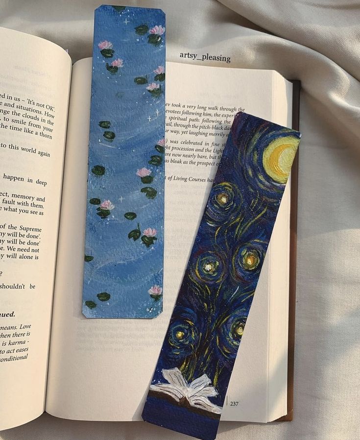 an open book with a tie on top of it next to a bookmark in the shape of a painting