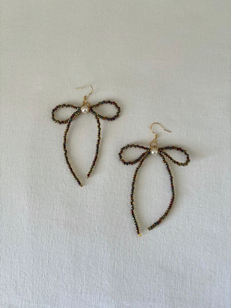 two pairs of earrings with bows on them sitting on top of a white cloth covered table