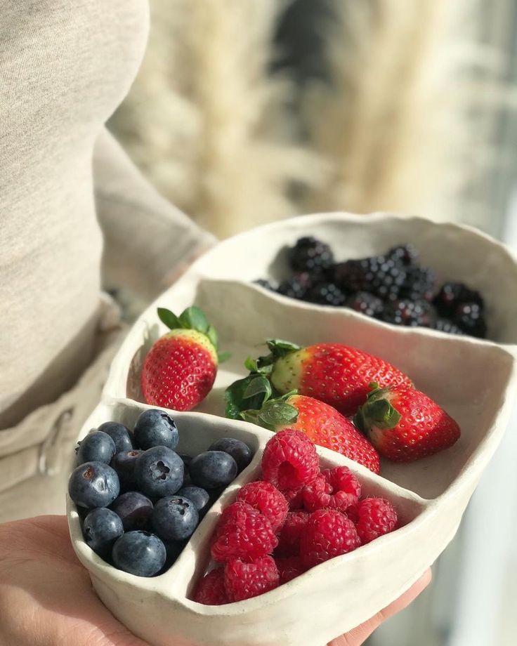 a person holding a bowl filled with berries and strawberries