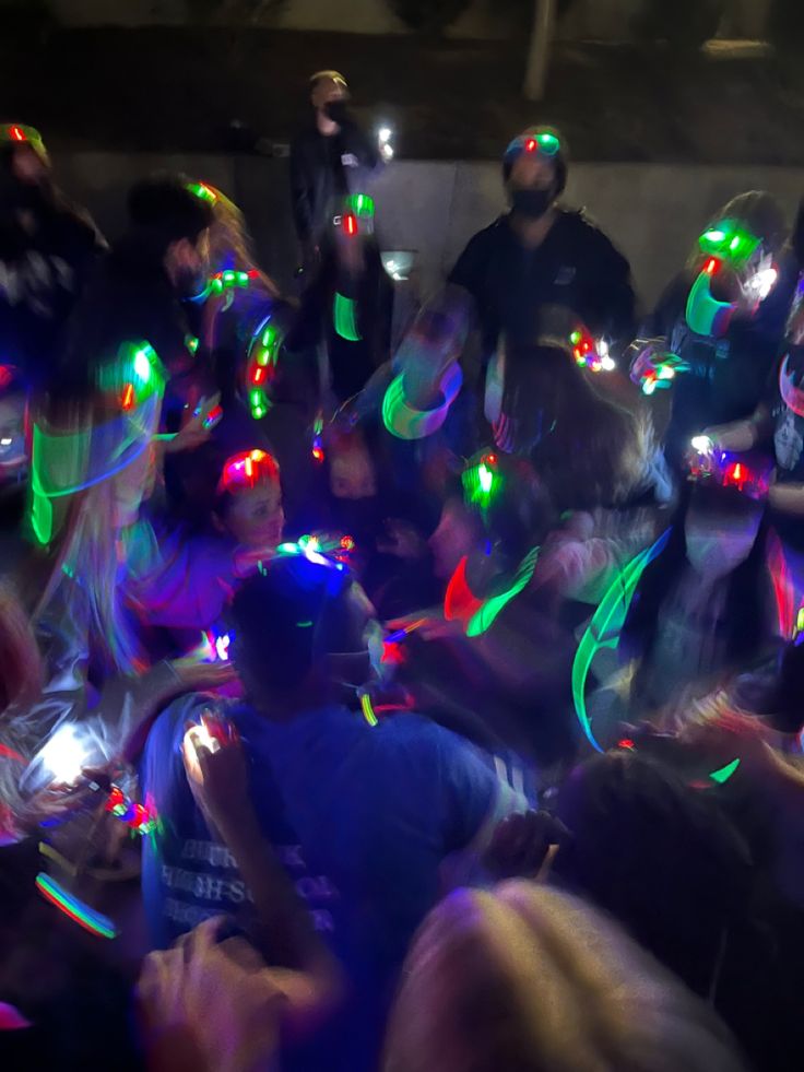 a group of people standing around each other with colorful lights on their heads and hands