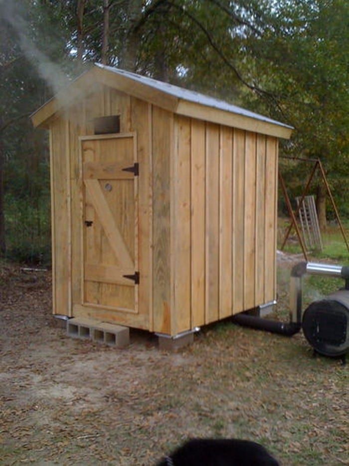 a small wooden outhouse sitting on top of a grass covered field next to a fire hydrant