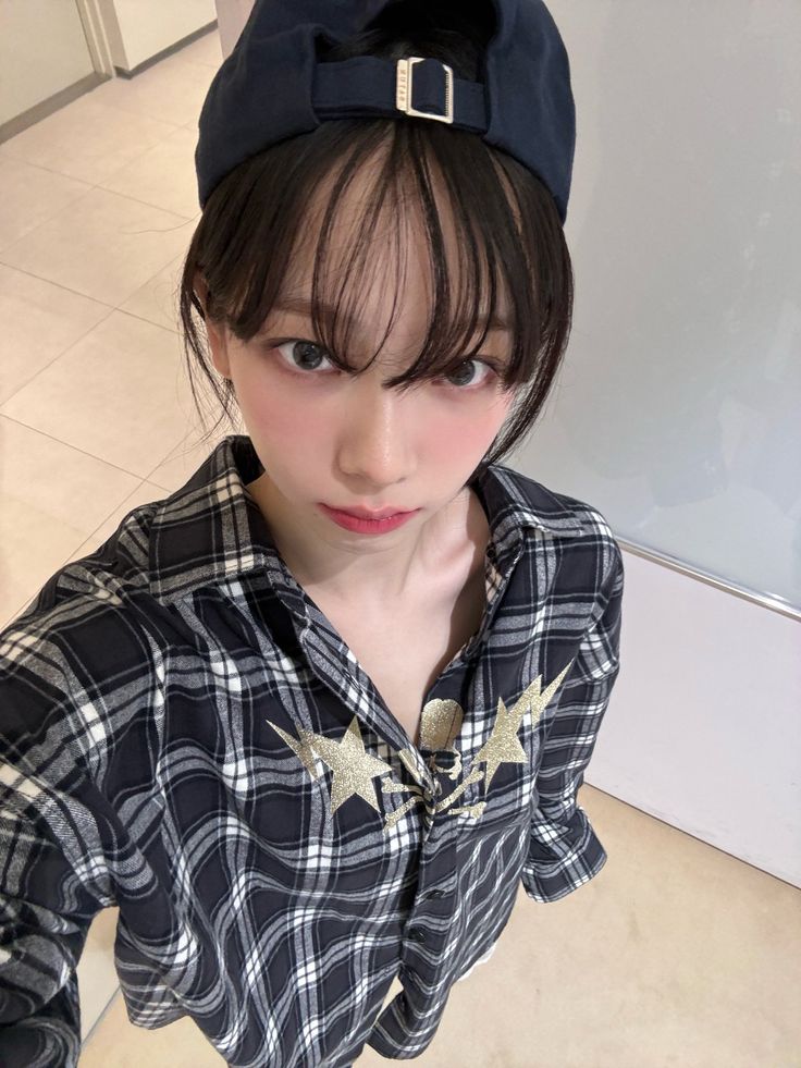 a girl with short hair wearing a black hat and plaid shirt looking at the camera