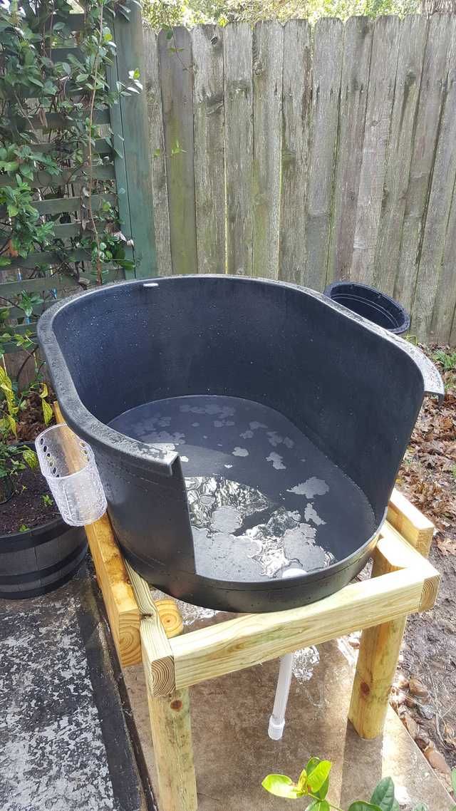 a large black tub sitting on top of a wooden table next to a fence and potted plants