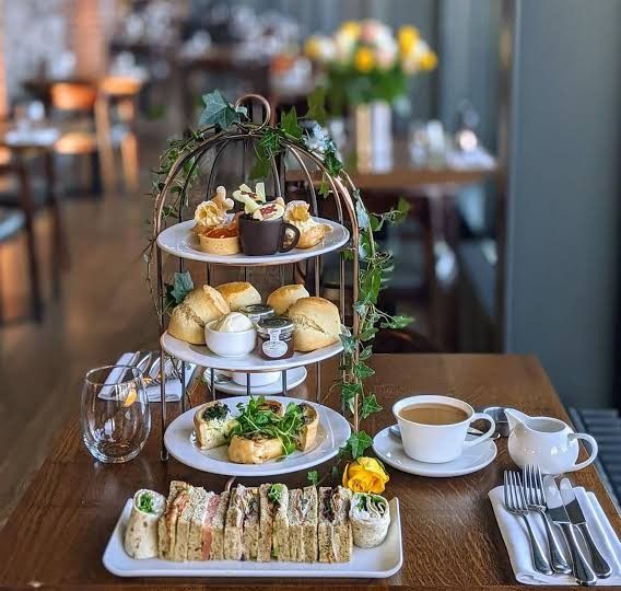 three tiered trays filled with food on top of a wooden table next to cups and saucers